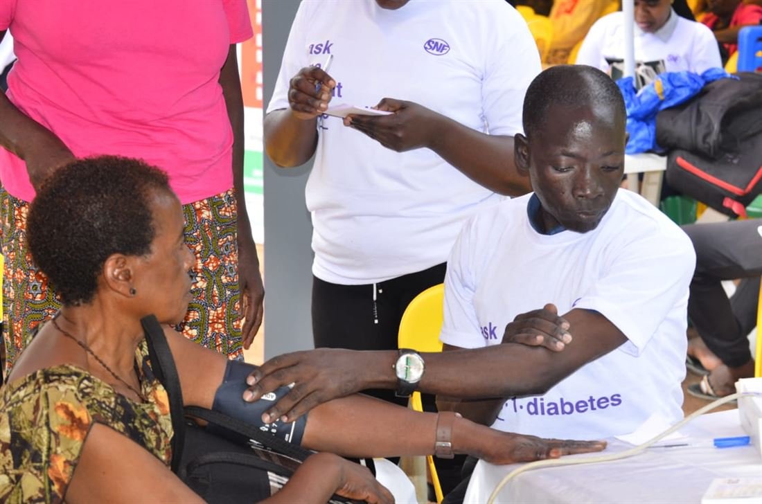 A health worker records a blood pressure measurement for a woman at a community health event.