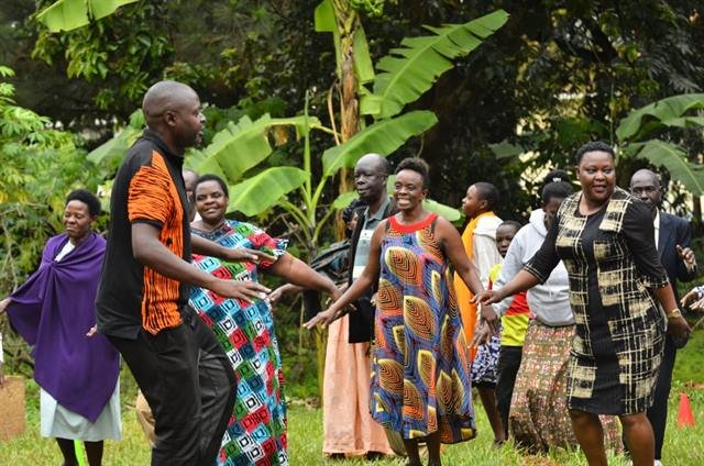 Community members join hands in a circle during a group activity outdoors.