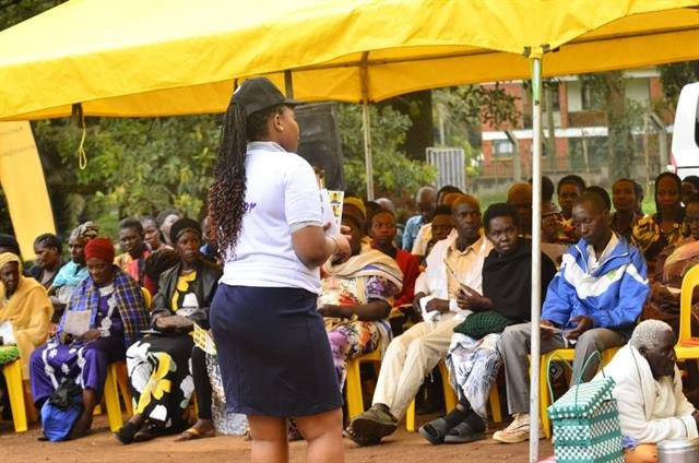 A facilitator addresses a large seated audience under an event tent.