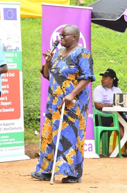 A woman speaks into a microphone at an outdoor health event, supported by a walking cane.