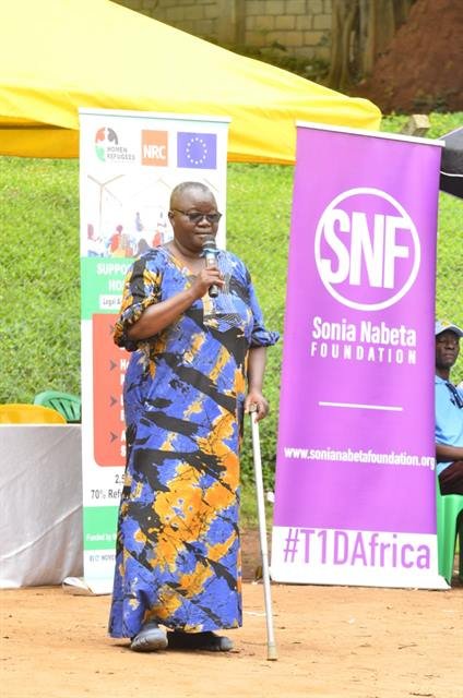 A woman supported by a walking cane speaks into a microphone at a public health event.