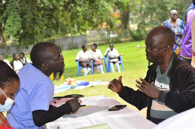 An RDAF health worker registers a community member at an outdoor screening table.