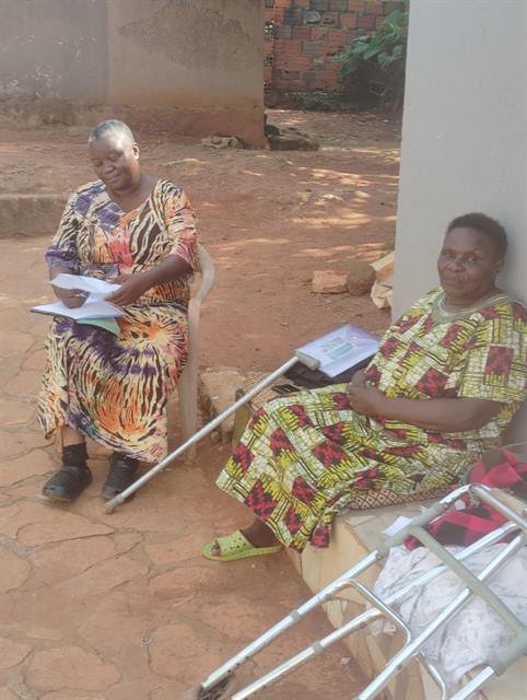 An RDAF team member sits with a community member and her walking frame outside a home.