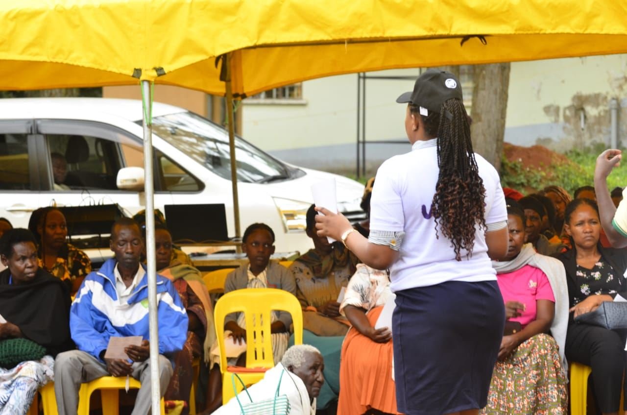 A facilitator addresses community members seated under an event tent at an RDAF session.